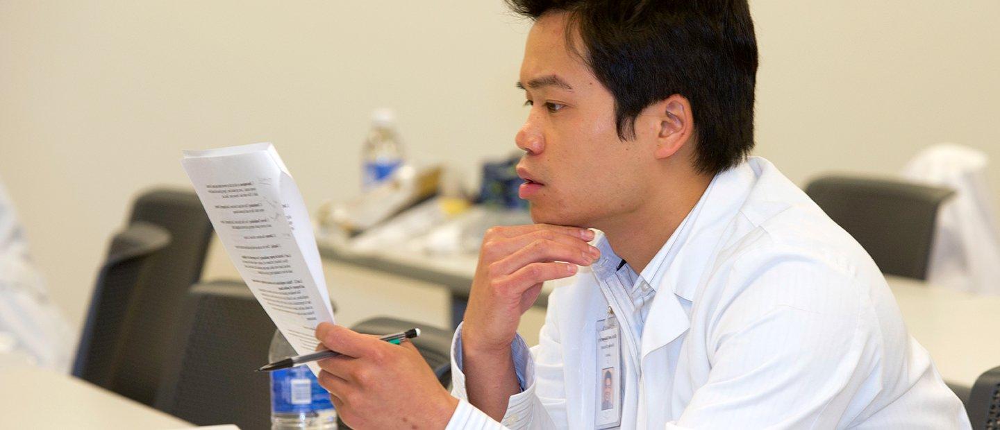 man in a white lab coat holding a pencil, looking over a form